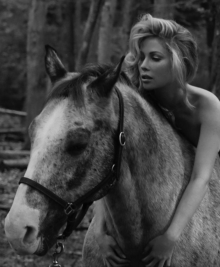 Black and white image of a woman embracing a horse in a forest setting.